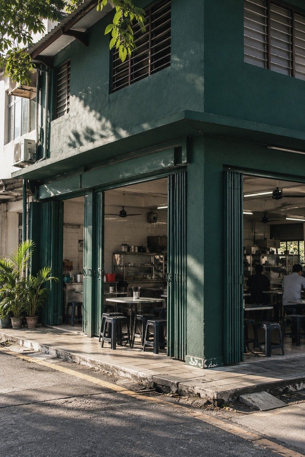 A kopitiam front at morning with a deep green menu board above the counter and marble tables